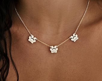 May include: Gold necklace with three paw print charms, each engraved with a name: 'Alfie', 'Mimi', and 'Rocky'.