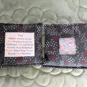 May include: Two black fabric pouches with a white and red pattern. One pouch has a clear window and the other has a label that reads "Find Ribbon Marble Arrow Star Airplane Duck Key Clothespin Bell Leaf Book Gummy Bear Basketball Button Heart Frog Flower Bicycle Dice Pom-Pom".