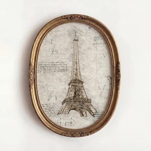 May include: An oval-shaped, gold-framed print featuring a sketch of the Eiffel Tower. The artwork is in sepia tones, with architectural details and handwritten notes surrounding the tower. The frame has ornate detailing.
