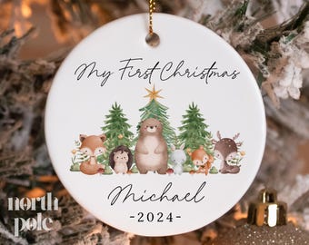 May include: White round Christmas ornament with a woodland animal theme. It says "My First Christmas Michael -2024-."  The ornament features a fox, hedgehog, bear, deer, and a squirrel.