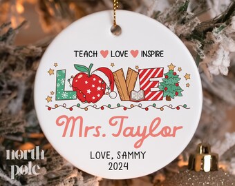 May include: White ceramic ornament with a red, green, and white "LOVE" design, surrounded by red and green lights. The text "Teach Love Inspire" is at the top, and "Mrs. Taylor LOVE, SAMMY 2024" is at the bottom.