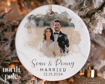 May include: A white round ornament with a watercolor design featuring a couple in a wedding photo. The text reads "Sean & Penny Married 12.15.2024".