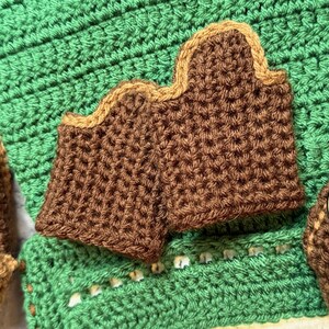 May include: Close-up of brown crochet pieces with a tan border, set against a green crochet background. The pieces have a textured appearance. The image showcases handmade crochet items, possibly for home decor or accessories.