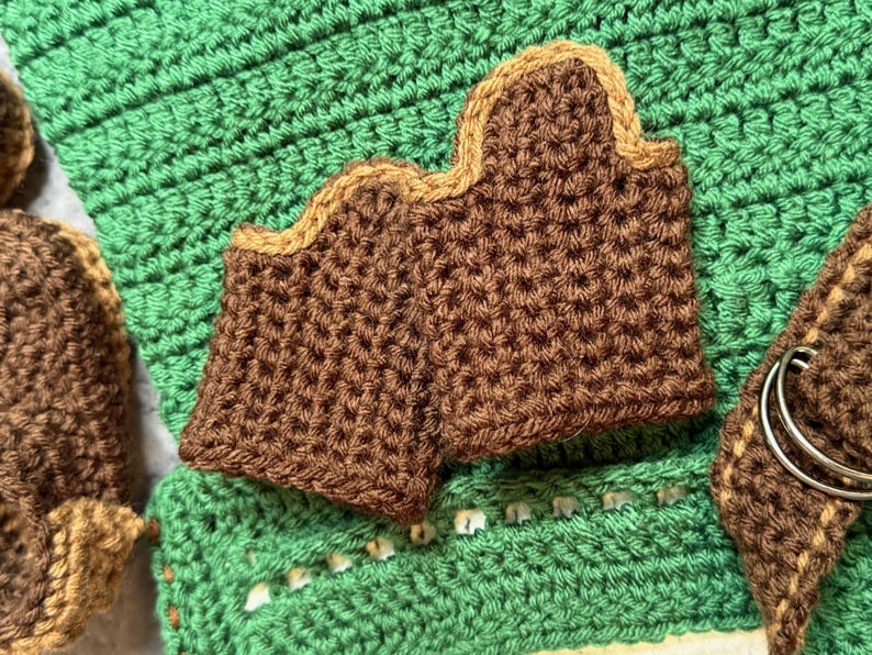 May include: Close-up of brown crochet pieces with a tan border, set against a green crochet background. The pieces have a textured appearance. The image showcases handmade crochet items, possibly for home decor or accessories.
