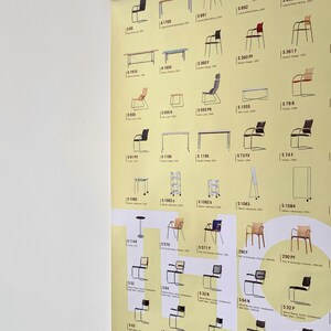Op de afbeelding: Een poster met een verzameling stoelontwerpen, elk gelabeld met een unieke code. De stoelen vari&euml;ren in stijl, kleur en materiaal, met onder andere hout, metaal en stof. De poster is gemonteerd met een houten frame, en de afmetingen zijn in centimeters.