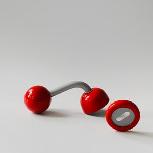 May include: A bottle opener featuring a curved grey handle connecting two glossy red spherical ends. One end is a solid red sphere, while the other is a red dome-shaped cap with a grey interior featuring an oval cutout for opening bottles.
