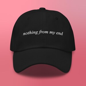 May include: Black baseball cap with the phrase "nothing from my end" embroidered in white. The cap has a curved brim and a button on top. The hat is set against a pink background.