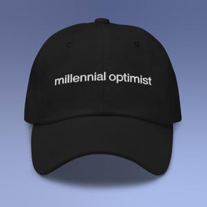 May include: Black baseball cap with the embroidered text "millennial optimist" in white. The cap has a curved brim and a structured fit. The hat is a classic style, suitable for casual wear.