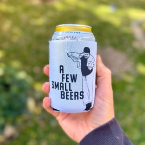 Puede incluir: Un enfriador de latas de cerveza blanco con el texto "A FEW SMALL BEERS" y una ilustración en blanco y negro de un hombre. El enfriador está envuelto alrededor de una lata de cerveza importada.