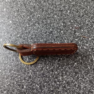 May include: A brown leather keychain with a brass key ring. The leather is stitched with a decorative pattern.