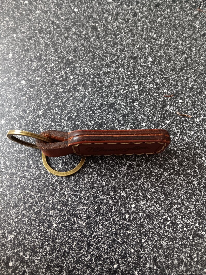 May include: A brown leather keychain with a brass key ring. The leather is stitched with a decorative pattern.