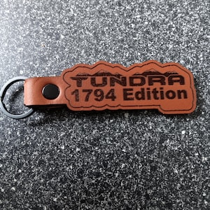 May include: Brown leather keychain with a black metal ring. The keychain has the text "Tundra 1794 Edition" embossed on it.