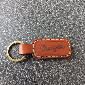 May include: Brown leather keychain with a brass ring and the word "Wrangler" embossed in white stitching.