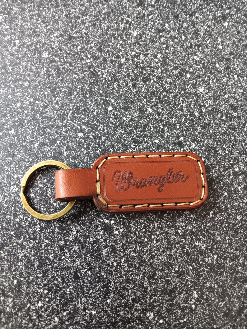 May include: Brown leather keychain with a brass ring and the word "Wrangler" embossed in white stitching.