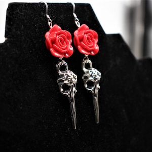 May include: A pair of silver earrings with a red rose charm and a bird skull pendant.