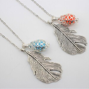 May include: Two silver necklaces with feather pendants. One necklace has a light blue cage charm and the other has an orange cage charm.