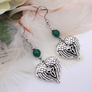 May include: Silver heart-shaped earrings with green gemstone beads and a Celtic knot design. The earrings are hanging from silver hooks.