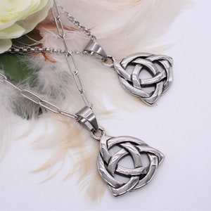 Può includere: Due collane d'argento con ciondoli a nodo celtico. Le collane sono su uno sfondo bianco con piume bianche.