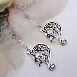 Peut inclure: Boucles d'oreilles en argent avec un nœud celtique et une perle d'opale blanche. Les boucles d'oreilles présentent un motif détaillé d'une tête de loup.