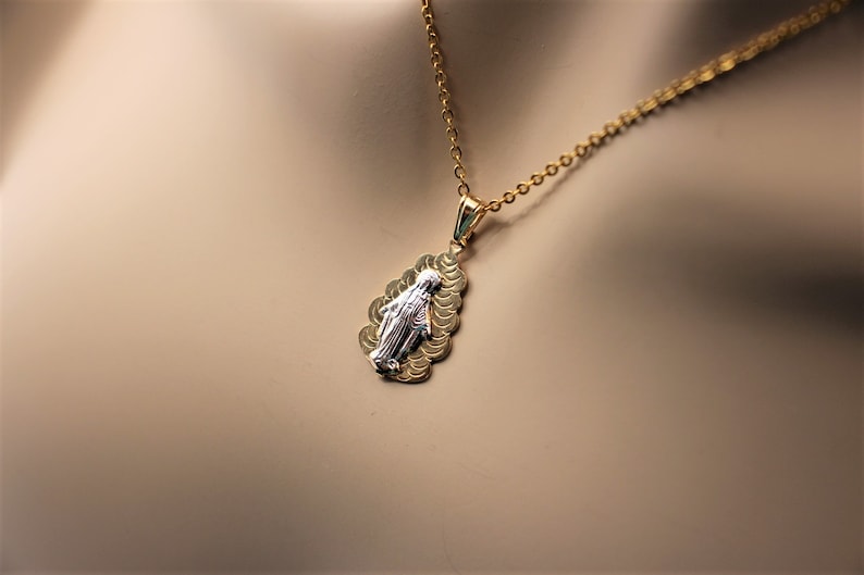 K&ouml;nnte beinhalten: Goldkette mit einem Anh&auml;nger, der ein zweifarbiges Bild der Jungfrau Maria zeigt. Der Anh&auml;nger ist tropfenf&ouml;rmig und hat ein strukturiertes Design.