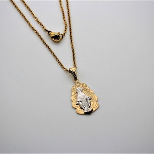 K&ouml;nnte beinhalten: Eine goldene Kettenkette mit einem Anh&auml;nger, der ein silbernes Bild der Jungfrau Maria zeigt. Der Anh&auml;nger ist von einem goldenen Design umgeben.
