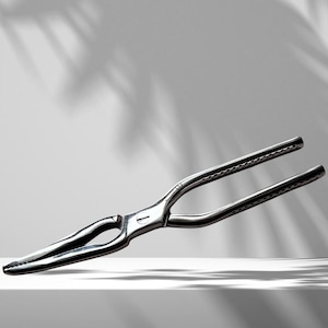 May include: A silver crab cracker with a textured handle. The cracker is open and appears to be made of metal.