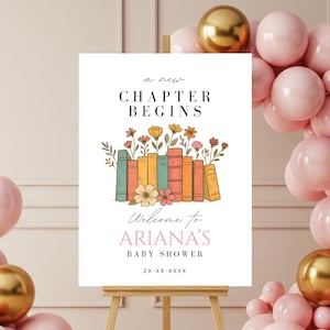 May include: A white sign on a wooden easel with the text "A New Chapter Begins" and "Welcome to Ariana's Baby Shower". The sign features a floral and book design. Pink and gold balloons decorate the background.