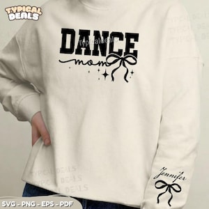 May include: A cream-coloured sweatshirt with the words "DANCE mom" in black, featuring a bow and stars design. The name "Jennifer" is printed on the sleeve, along with a bow. The sweatshirt has a crew neck and long sleeves.