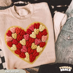 Puede incluir: Sudadera beige claro con un diseño de corazón. El corazón está compuesto por corazones tejidos en rojo, rosa y crema, sobre un fondo dorado con purpurina. El texto "Typicaldeals" es visible. Una chaqueta vaquera es parcialmente visible.