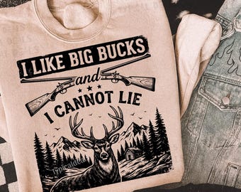 Puede incluir: Sudadera beige con el texto "I LIKE BIG BUCKS and I CANNOT LIE" sobre un gráfico de un ciervo, rifles, montañas y árboles. Una chaqueta vaquera está al lado.