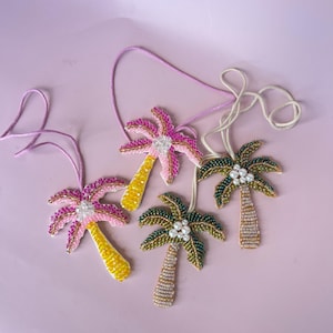 Op de afbeelding: Vier kralen palmboomornamenten met roze, gele en groene accenten. Elk ornament heeft een touwtje om op te hangen. De palmbomen hebben kralenstammen en bladeren, sommige met parelachtige kralen.