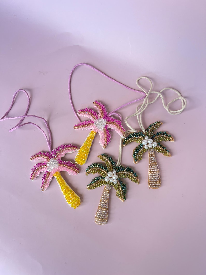 Op de afbeelding: Vier kralen palmboomornamenten met roze, gele en groene accenten. Elk ornament heeft een touwtje om op te hangen. De palmbomen hebben kralenstammen en bladeren, sommige met parelachtige kralen.