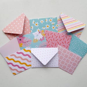 May include: A selection of small, patterned envelopes in a variety of colours. Designs include hearts, daisies, stripes, dots, and floral prints. The envelopes are arranged on a light surface, displaying their diverse designs.