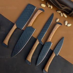 May include: A set of six kitchen knives with dark blades and wooden handles. The blades have a textured finish. The handles are light brown with a dark end cap. A brown leather sheath is visible in the background.