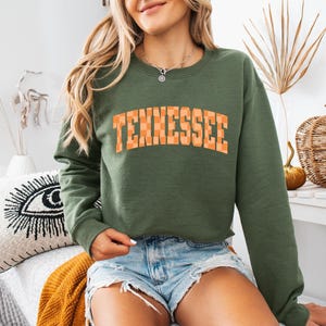 a woman sitting on a bed wearing a sweatshirt that says tennessee