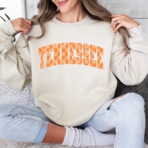 a woman sitting on a couch wearing a sweatshirt that says tennessee