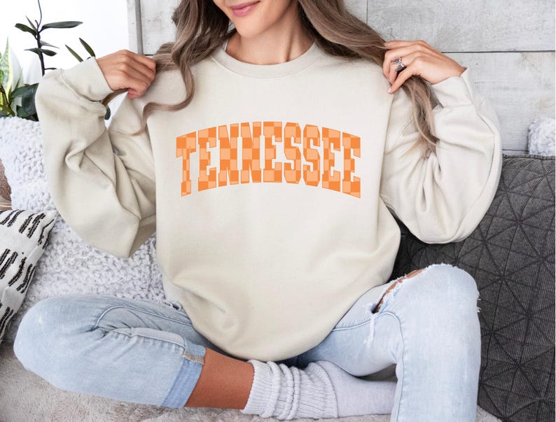 a woman sitting on a couch wearing a sweatshirt that says tennessee