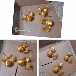 May include: Multiple golden Snitch replicas, from the Harry Potter series, are displayed on cardboard. Each Snitch has a spherical body and detailed wings. The objects are painted in a metallic gold colour, and are likely handmade.