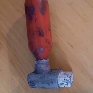 May include: A red and gray valve with a cylindrical red top and a gray, rectangular base. The red top has dark spots. The valve is likely used for controlling the flow of fluids or gases.