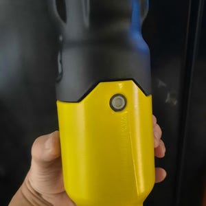 May include: A cylindrical object with a yellow body and a black top. The object has a button and a small opening. The item is held in a hand.