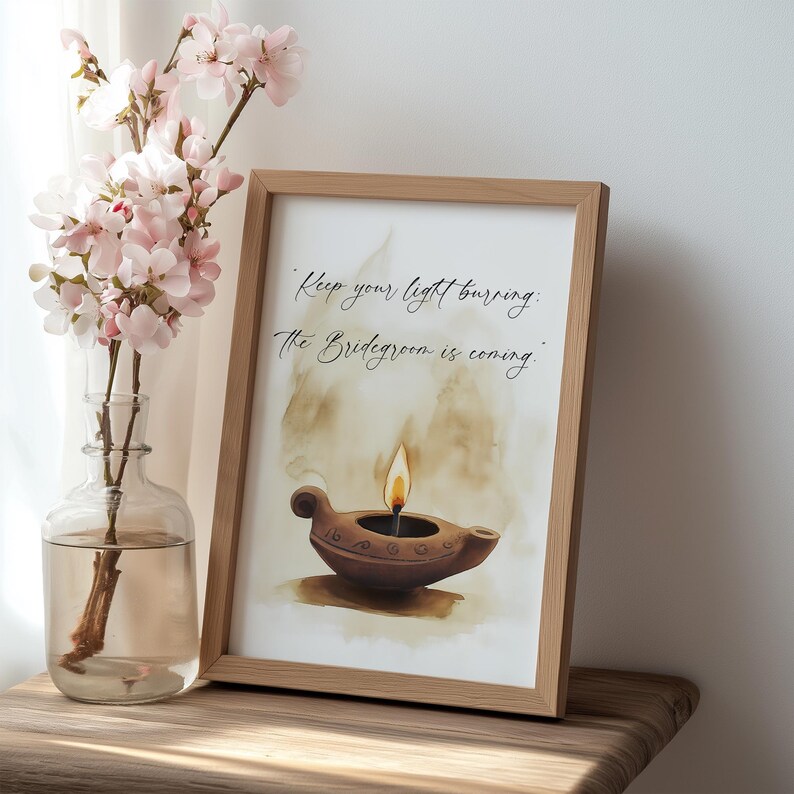 May include: A framed print with the text "Keep your light burning. The Bridegroom is coming." The artwork features a watercolor illustration of a brown oil lamp with a lit flame. A glass vase with pink flowers is to the left.