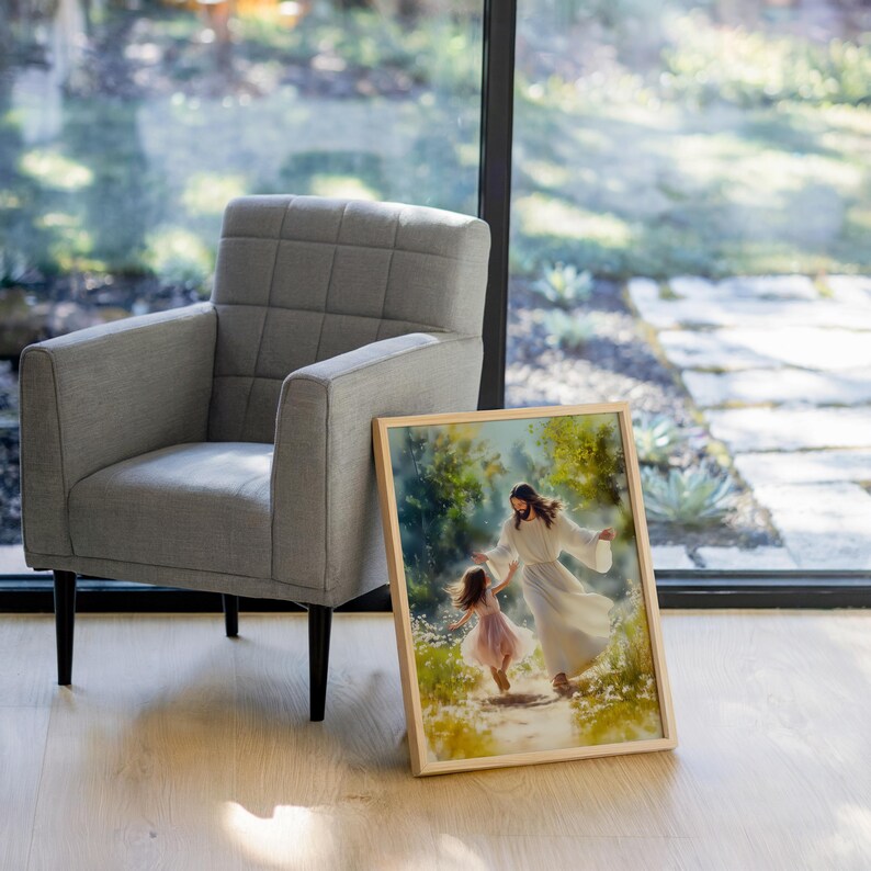 May include: A framed art print shows a figure in a white robe guiding a young girl in a pink dress along a path. The artwork is set in a natural, outdoor scene with soft lighting. A grey armchair with black legs is to the left.