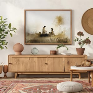 May include: A watercolor painting of two figures sitting by a well, framed in a wooden frame and hanging on a white wall above a wooden cabinet. The painting is set against a light brown background with a tree in the background.