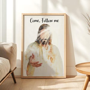 Peut inclure: Une peinture à l'aquarelle de Jésus-Christ portant une robe blanche et une auréole. La peinture est encadrée dans un cadre en bois clair et porte le texte "Come, Follow me" en haut.