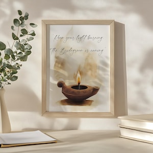 May include: Framed print featuring a watercolor illustration of a brown oil lamp with a lit flame. The artwork includes the text "Keep your light burning: The Bridegroom is coming." The frame is made of light-colored wood.