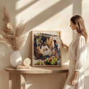 May include: A watercolor painting depicting a scene from the Bible. Three people are seated at a table, with a woman standing nearby. The painting is framed in a wooden frame and is hanging on a wall.