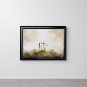 Op de afbeelding: Een ingelijst schilderij dat drie kruisen toont die gesilhouetteerd zijn tegen een wazige, gouden lucht. De kruisen staan ​​op de achtergrond van een heuvel en een grasveld.