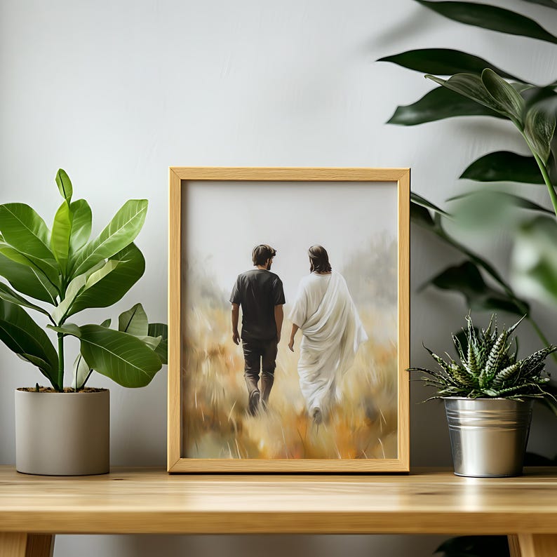 May include: A framed painting of two figures walking away from the viewer in a field. The figure on the left is wearing a black shirt and jeans, while the figure on the right is wearing a white robe. The painting is set against a light brown background.