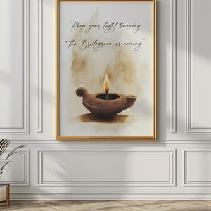 May include: A framed art print featuring a watercolor painting of a brown oil lamp with a lit flame. The artwork includes the text "Keep your light burning: The Bridegroom is coming." The frame is gold, and the background is a soft, neutral color.
