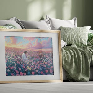 May include: A framed painting of a person sitting in a field of pink, purple, and white flowers. The sky is a soft pink and blue with clouds. The painting is in a light wood frame.
